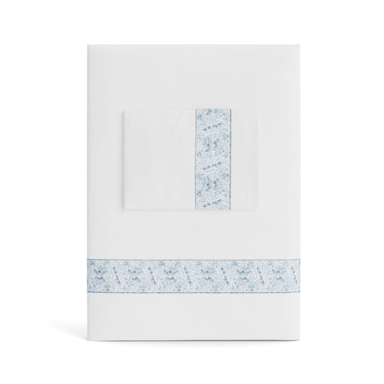 A folded white Minaudiere Sheet Set by Judith Leiber Couture x Ann Gish, shown with its matching pillowcase on top, featuring a light blue sequenced border band that mirrors the jeweled sparkle of the Minaudiere design. - SSMIK-WHI-BLE SSMIQ-WHI-BLE